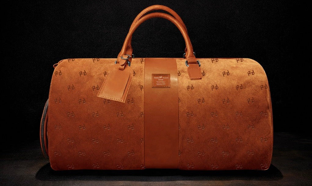 Orange suede duffel bag with embossed pattern on a black background